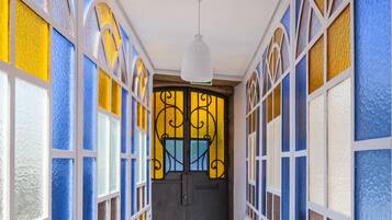 Un couloir étroit avec un escalier menant à une porte sombre, de part et d’autre de laquelle se trouvent des murs ornés de vitraux aux couleurs vives.