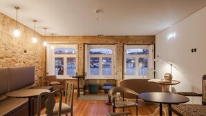 Un interior acogedor con una pared de piedra, piso de madera y un área de estar con mesas y sillas.