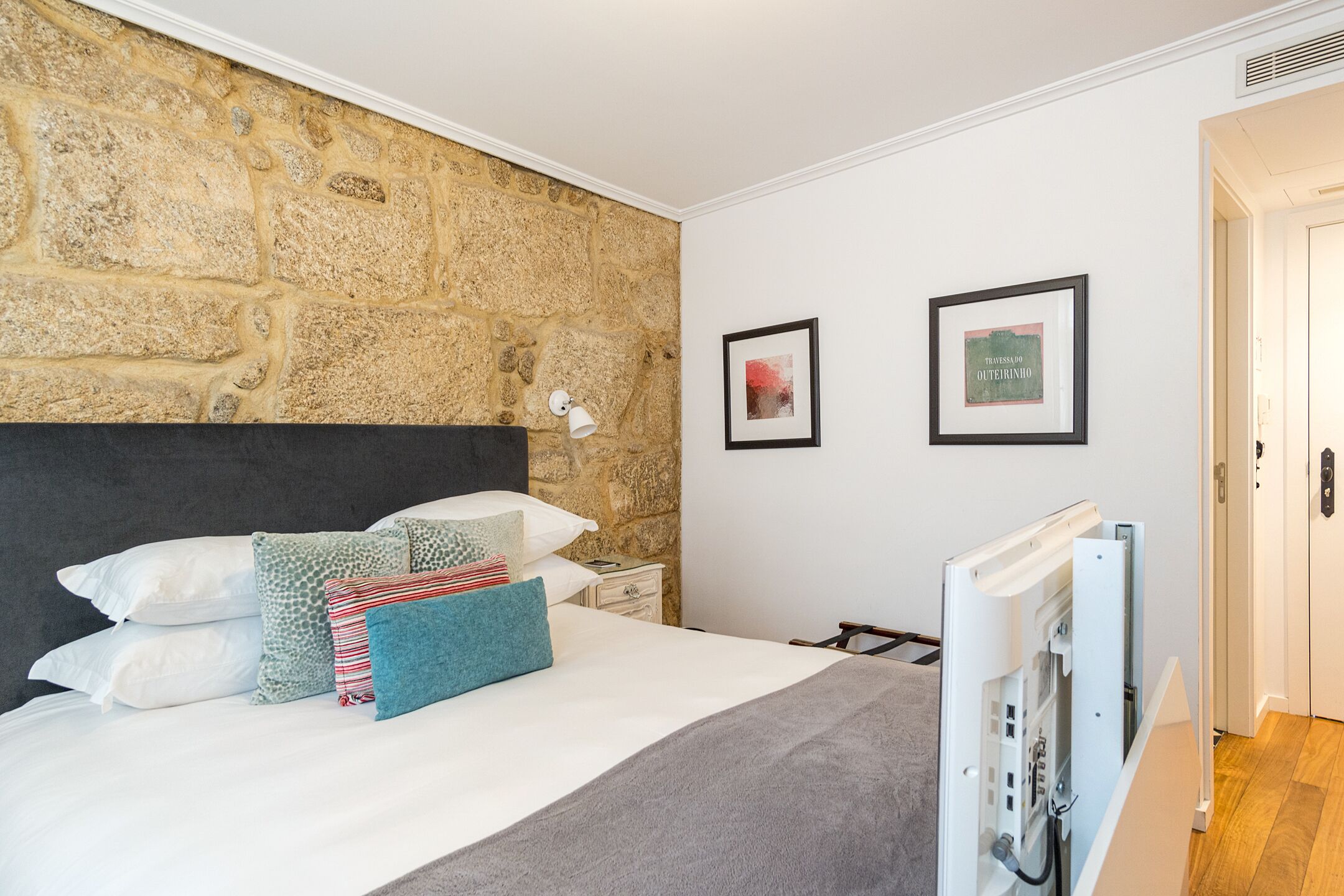 Una camera da letto con parete in pietra, un letto con molti cuscini, un comodino e due quadri appesi al muro.