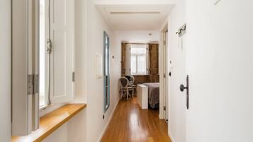 A narrow hallway with wooden flooring, white walls, and a small seating area with a chair and table.