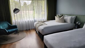A hotel room with a bed, two bedside tables, a chair, a floor lamp, and a view of trees through sheer curtains. - Kyah Hotel (Blackheath)
