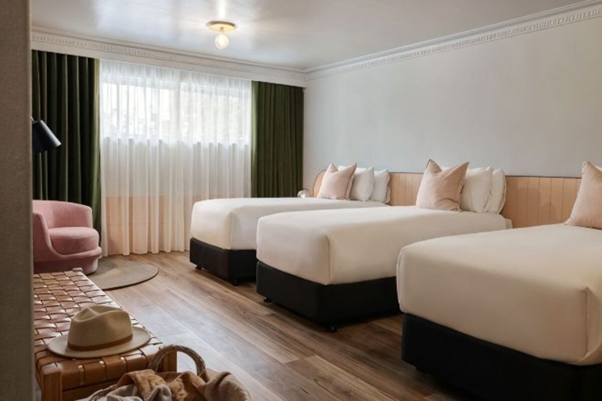 Une chambre d’hôtel avec deux lits, un bureau, une chaise et une fenêtre avec des rideaux.