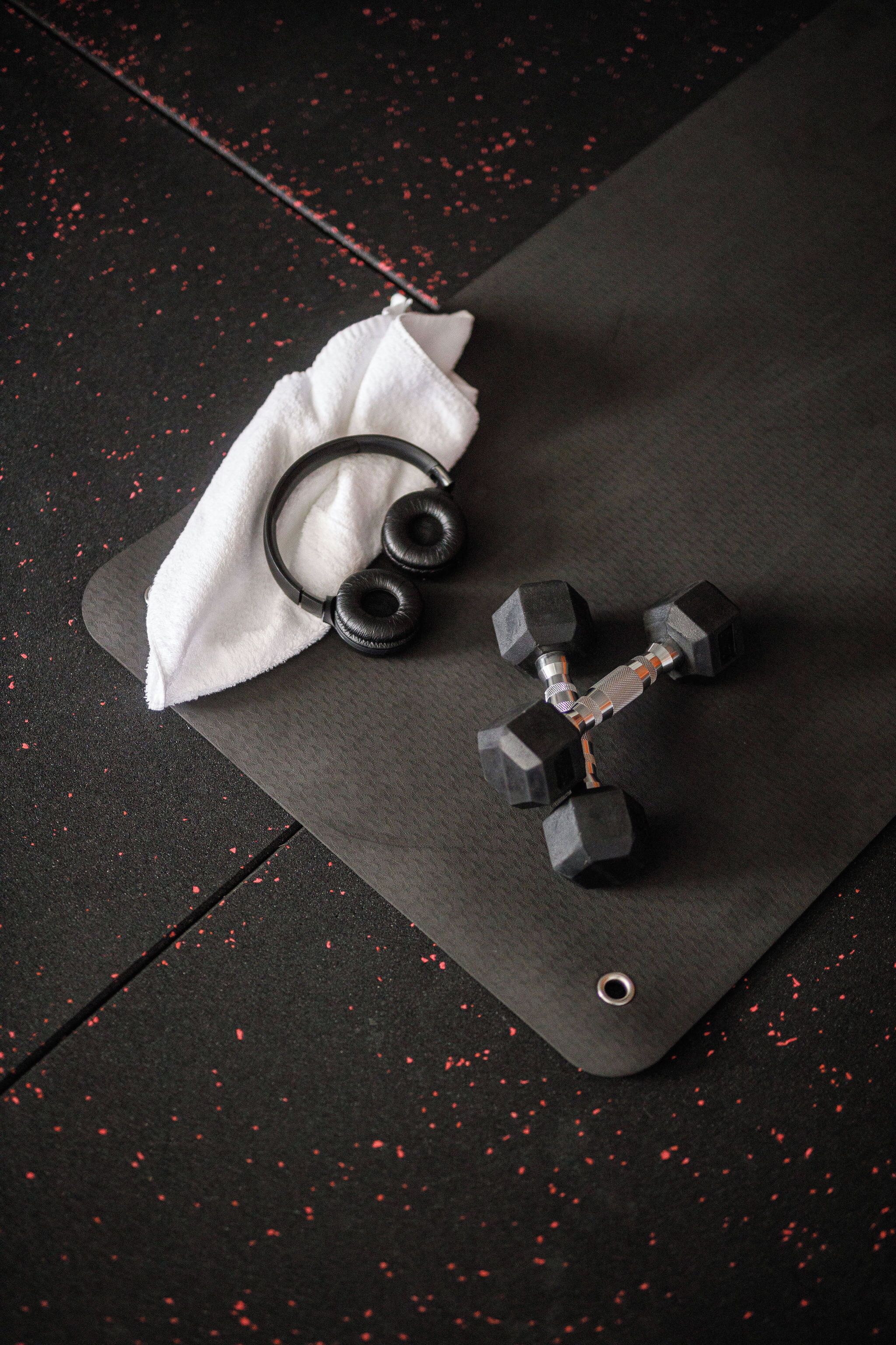 A black exercise mat with a white towel and black dumbbells on it.
