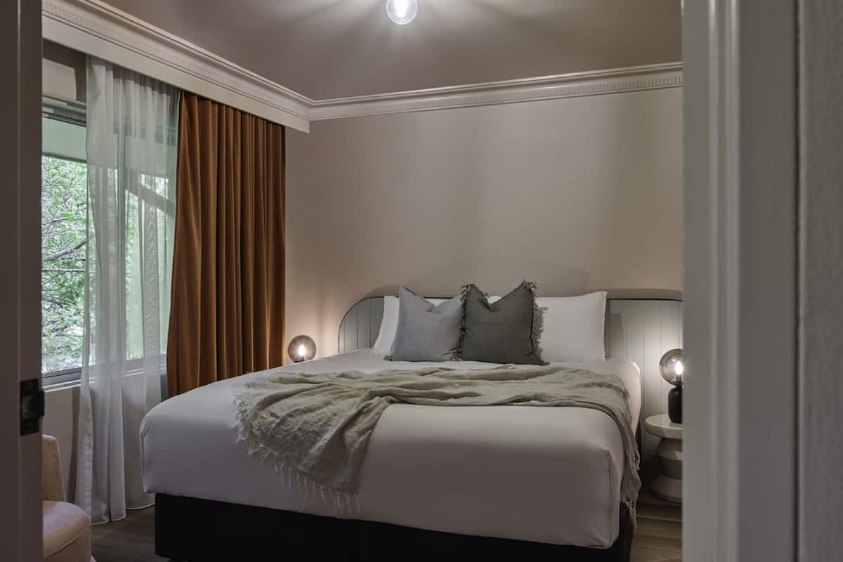 Een hotelkamer met een groot bed, twee bedlampen, een plafondlamp en een raam met gordijnen.