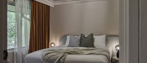 A hotel bedroom with a large bed, two bedside lamps, a ceiling light, and a window with curtains.
