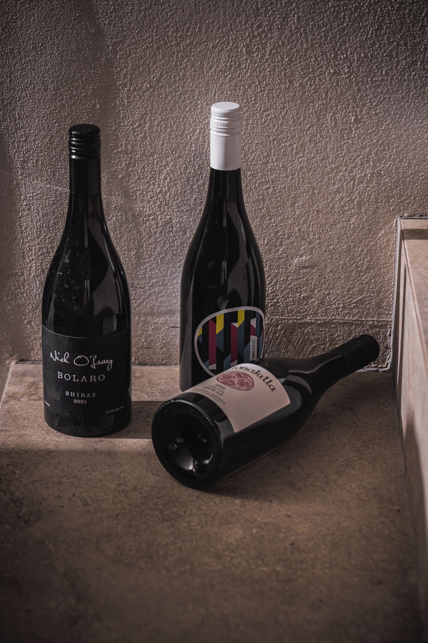 Two wine bottles on a stone ledge against a textured wall.
