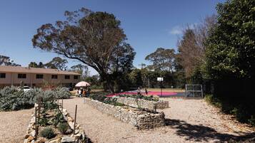 Un jardín con una cancha de baloncesto, un pabellón y un edificio al fondo.