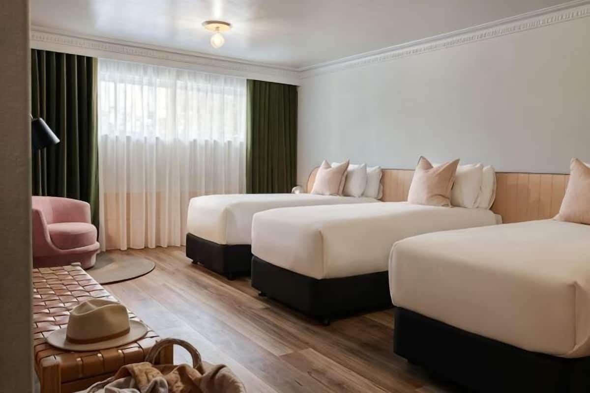 Een hotelkamer met twee bedden, een bureau, een stoel en een raam met gordijnen.