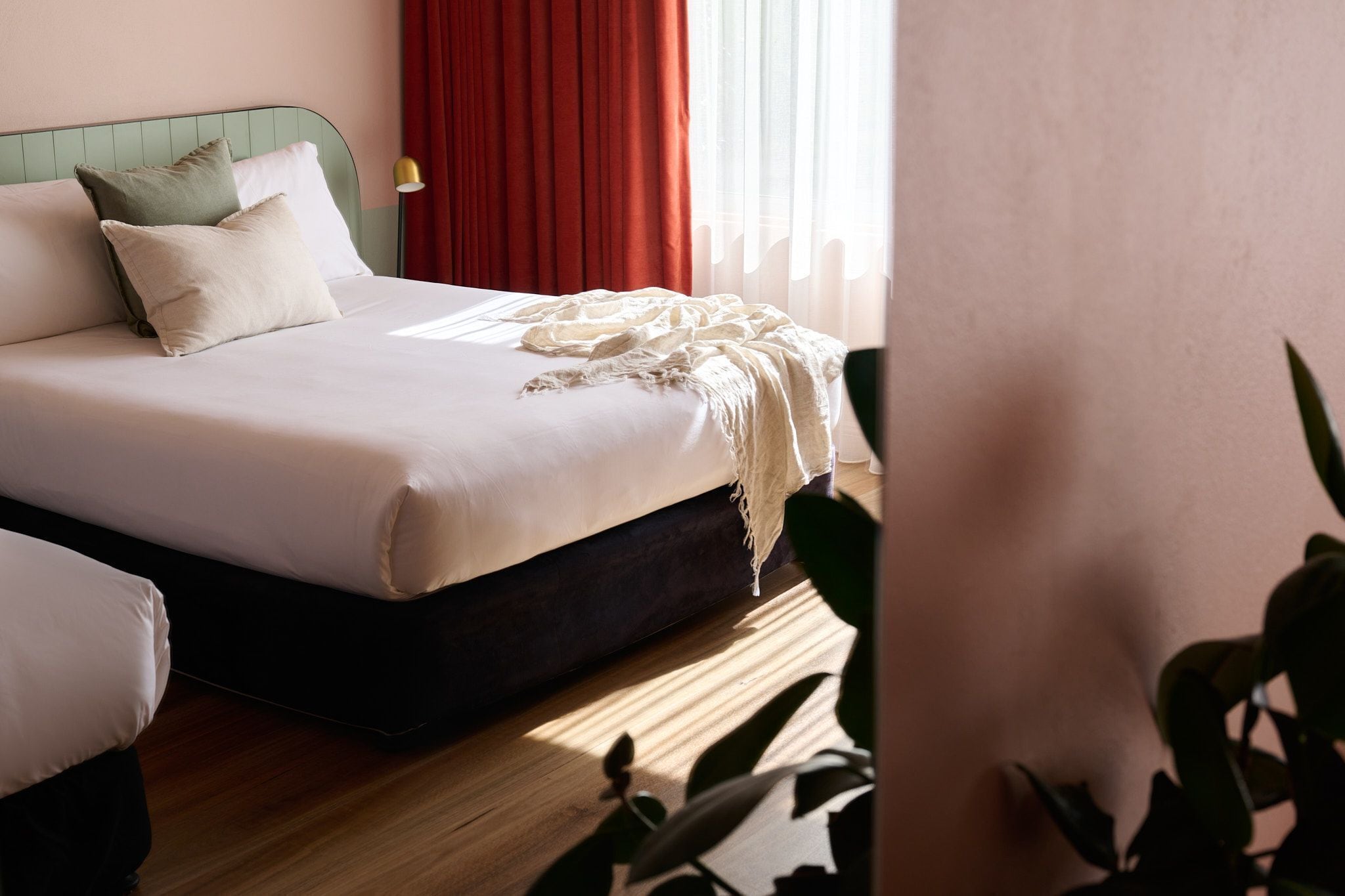 A neatly made bed with a white comforter and two pillows, a dark headboard, and a red curtain partially drawn.
