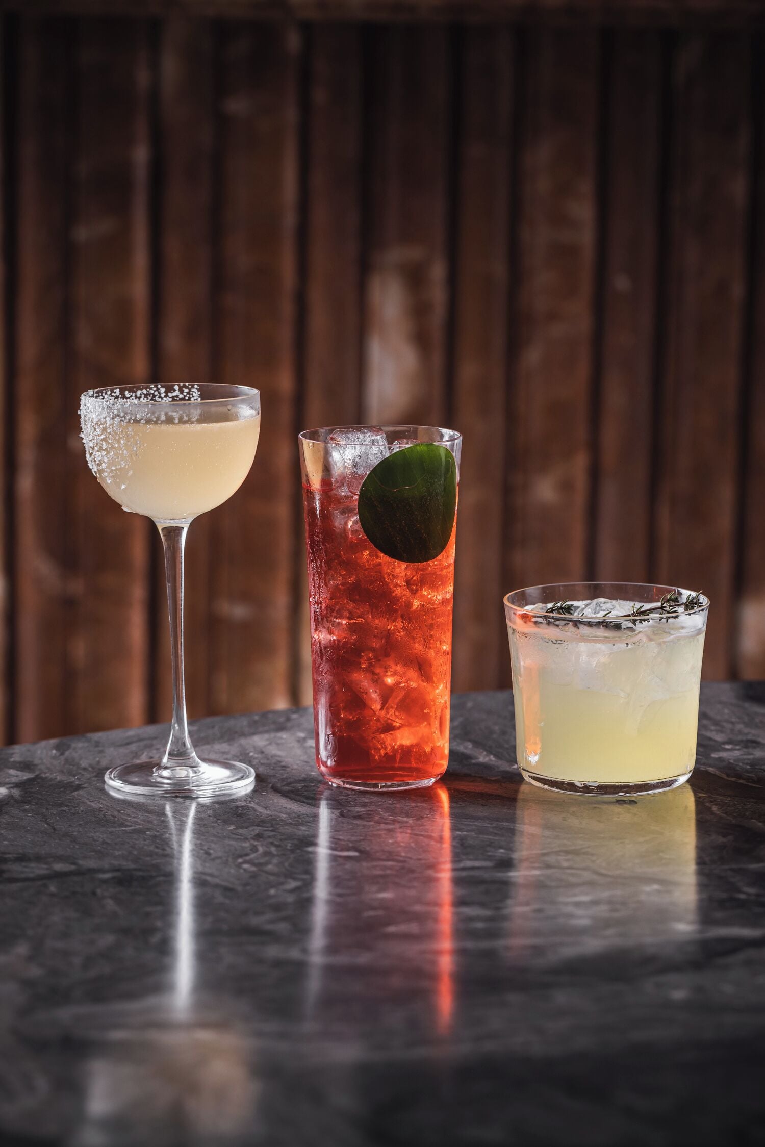Three different cocktails on a marble surface with a wooden background.