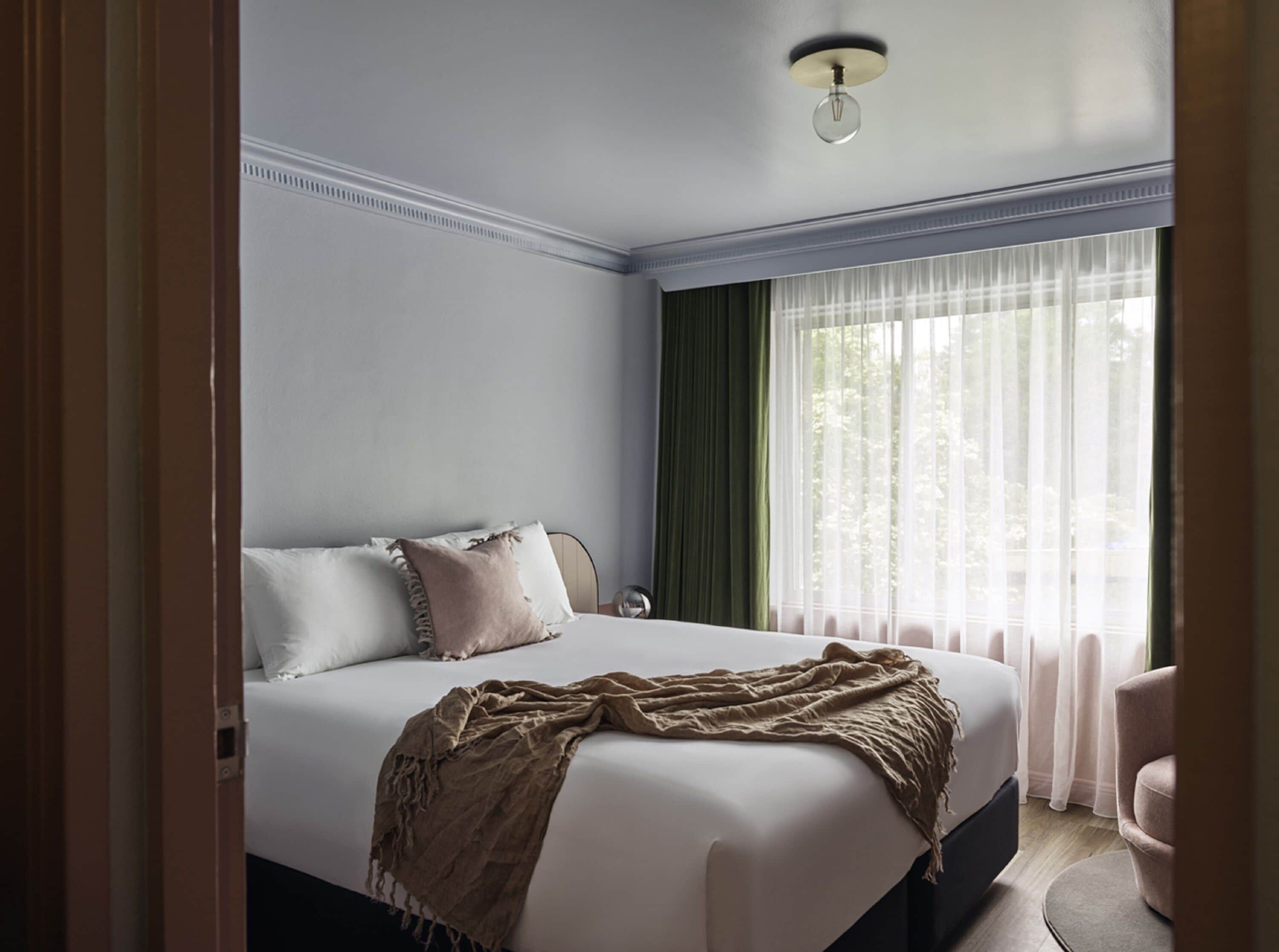 Un dormitorio con una cama grande, una mesita de noche, una lámpara y una ventana con cortinas.