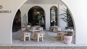 An outdoor seating area with wooden tables and chairs, potted plants, and a white wall with a sign. - Kyah Hotel (Blackheath)