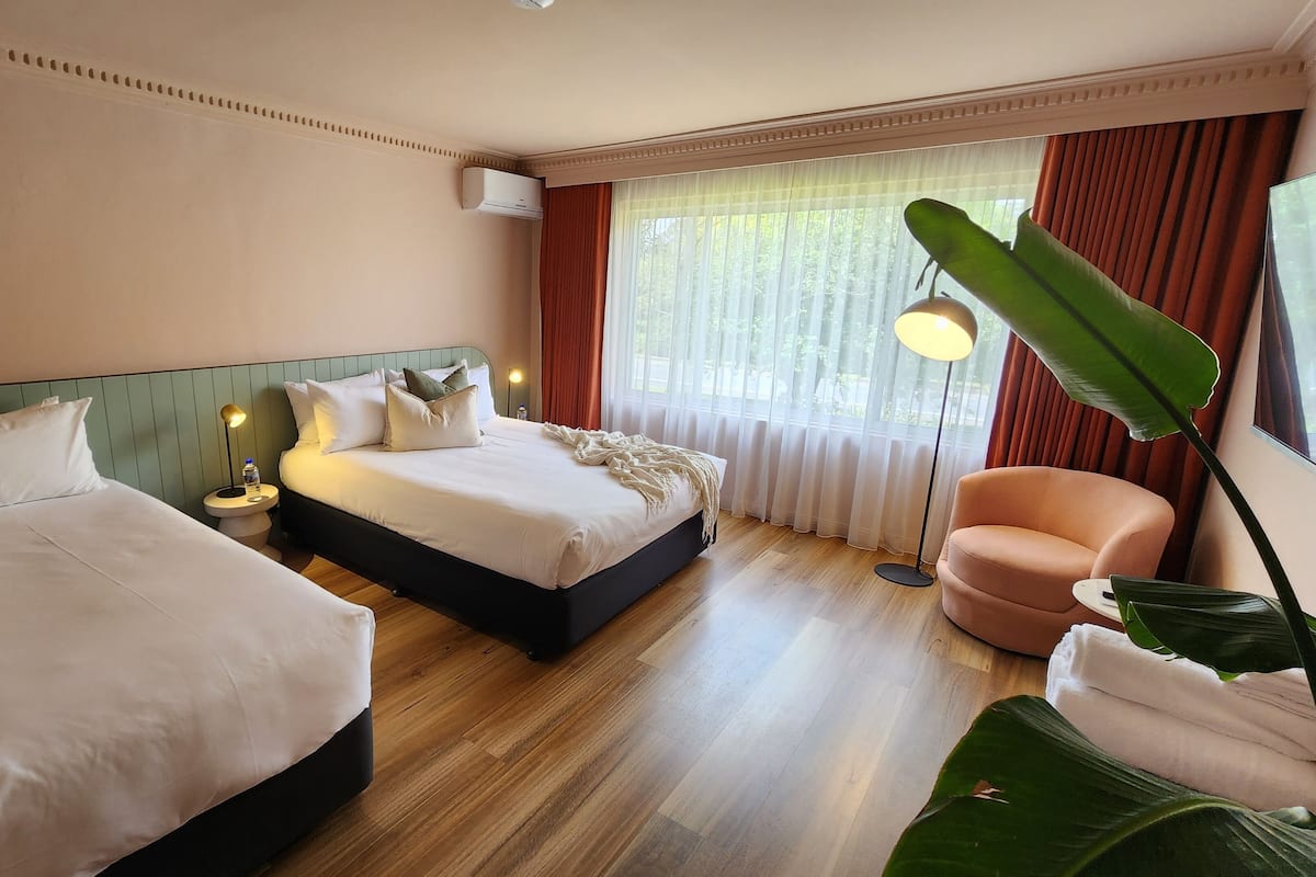 Een hotelkamer met twee bedden, een groot raam met gordijnen, een vloerlamp en een stoel.