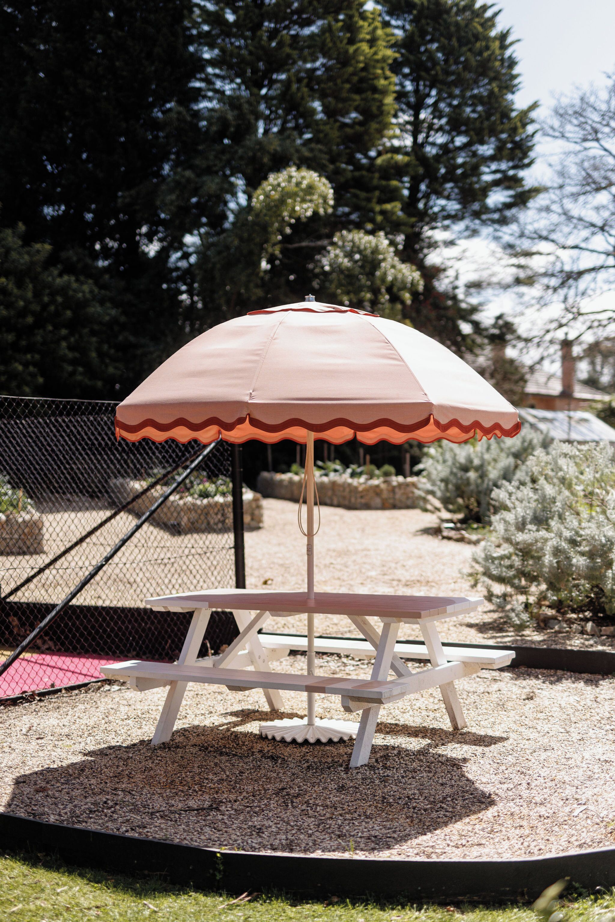 A picnic table with a white umbrella in a garden setting.