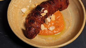 Um prato com uma salsicha grelhada e uma tigela de azeitonas.
