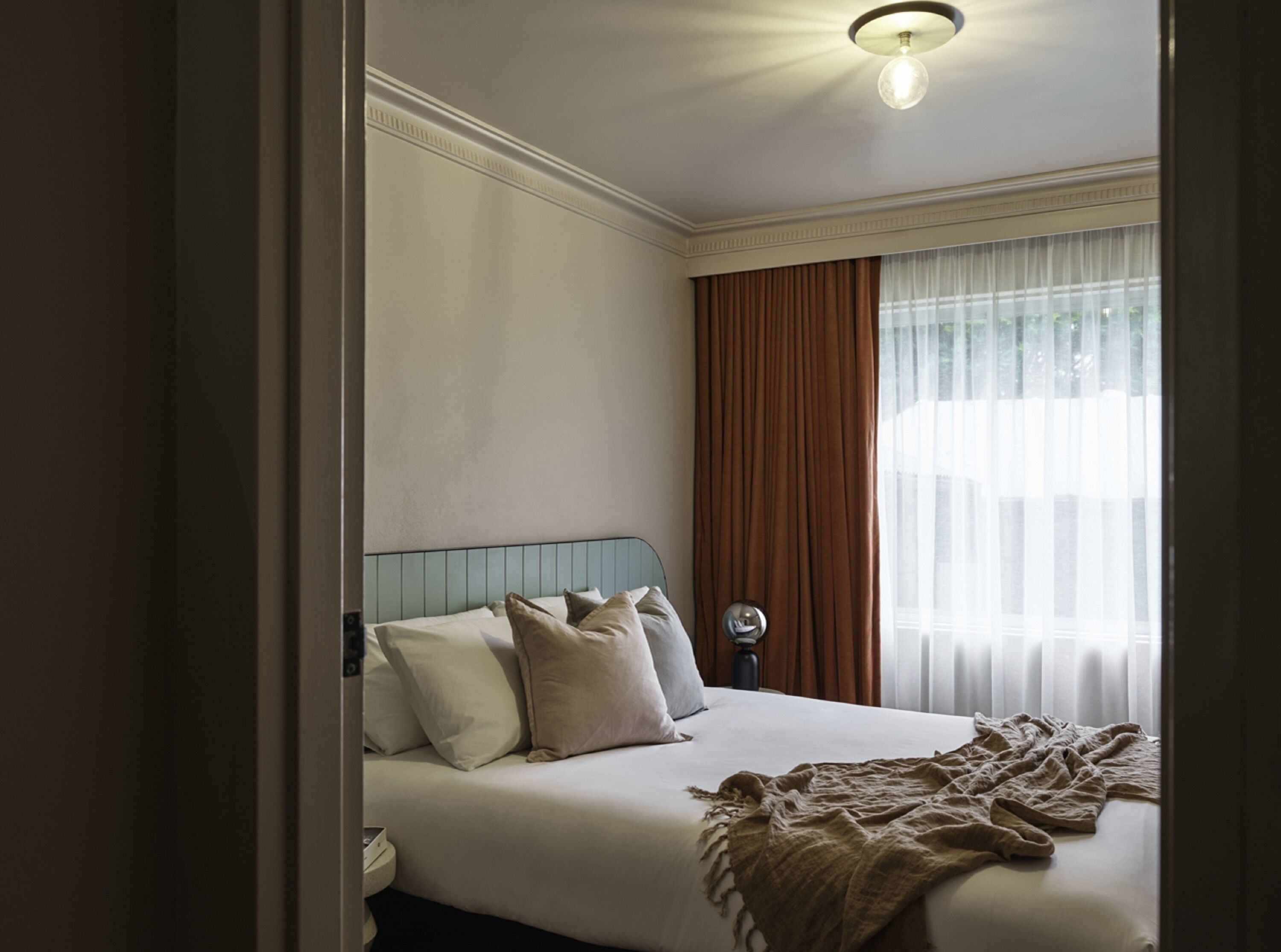 Habitación de hotel con una cama bien hecha, una mesita de noche y un ventanal con cortinas.
