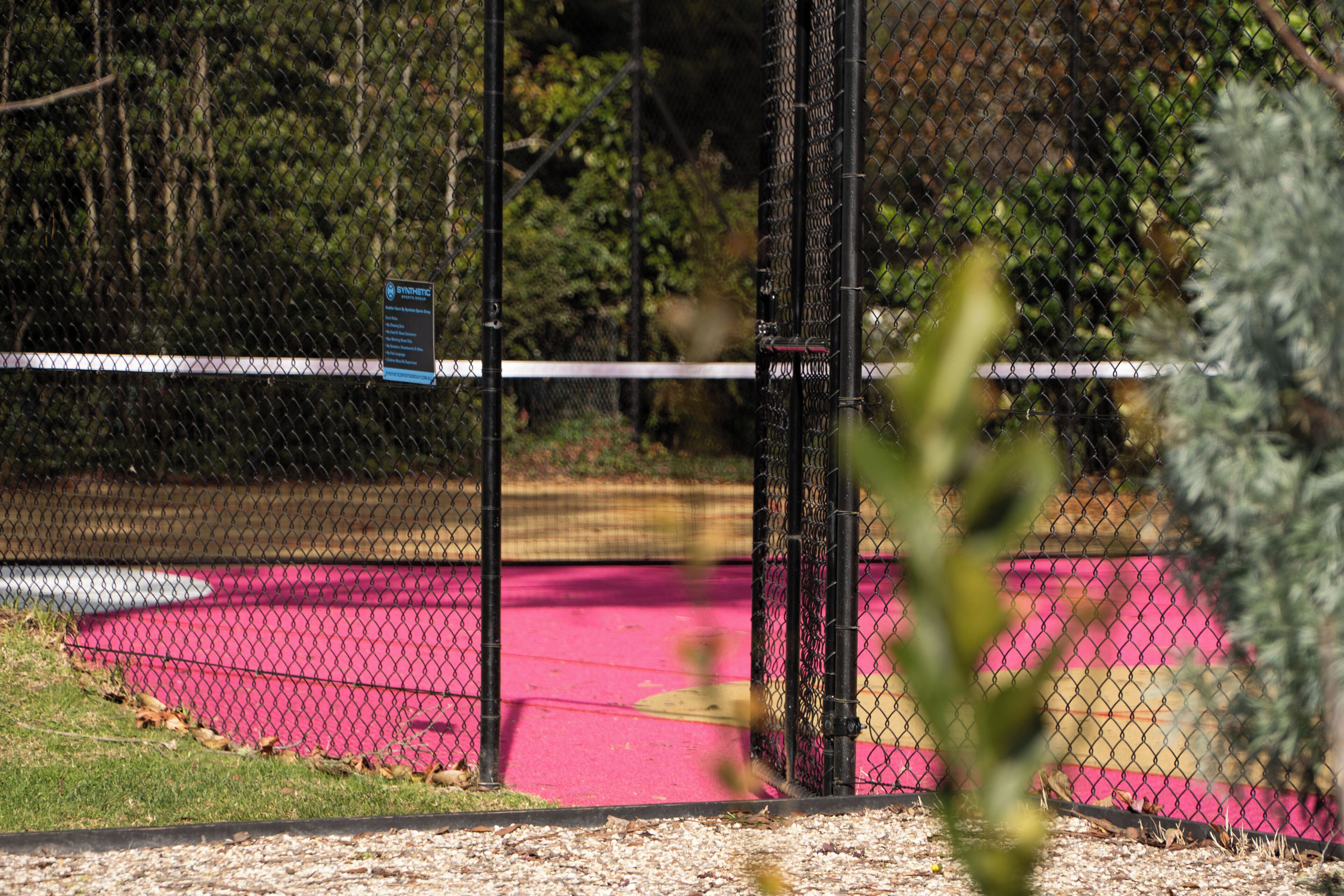 A fenced area with a sign, a pink surface, and greenery in the background.