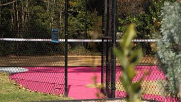 A fenced area with a sign, a pink surface, and greenery in the background.