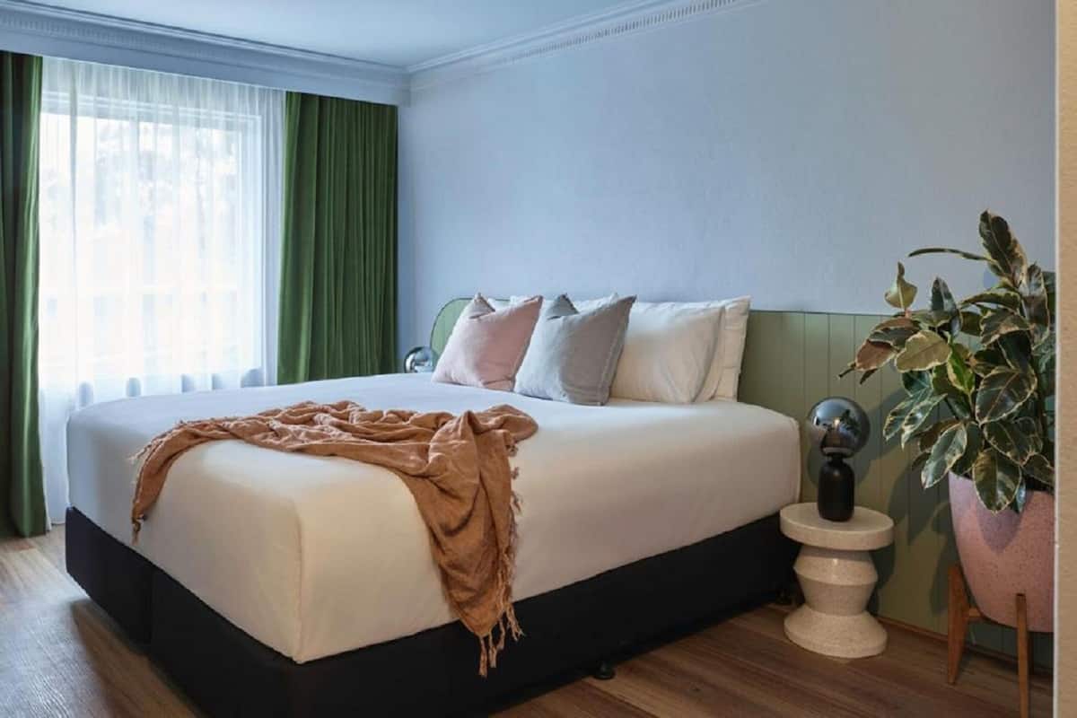 Een hotelkamer met een groot bed, een nachtkastje, een kamerplant en uitzicht op de stad.