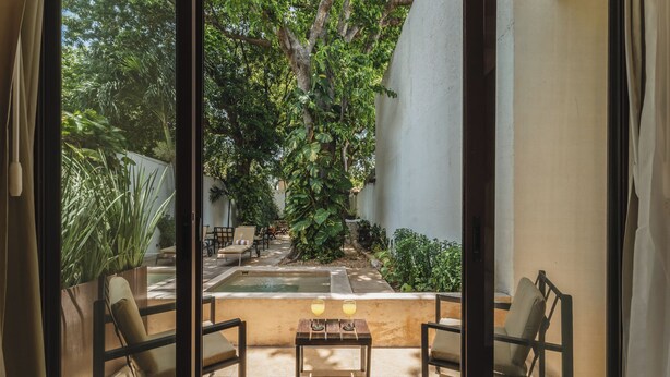 Une pièce donnant sur un jardin, avec une petite piscine et deux chaises disposées autour d’une table au centre.