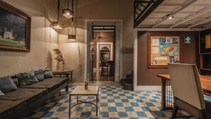 Un hall d’hôtel avec un sol à carreaux, un canapé, une table, une chaise, un tableau encadré et un panneau d’affichage.