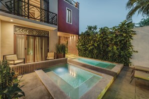 Een modern buitenzwembad met een zitgedeelte en een gebouw met een balkon.