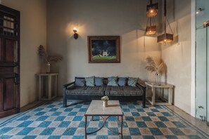 Een kamer met een zwart-wit geruite vloer, een bank met gestreepte kussens, een kleine tafel met een vaas, een aan de muur hangend schilderij, en hangende pendantlampen.