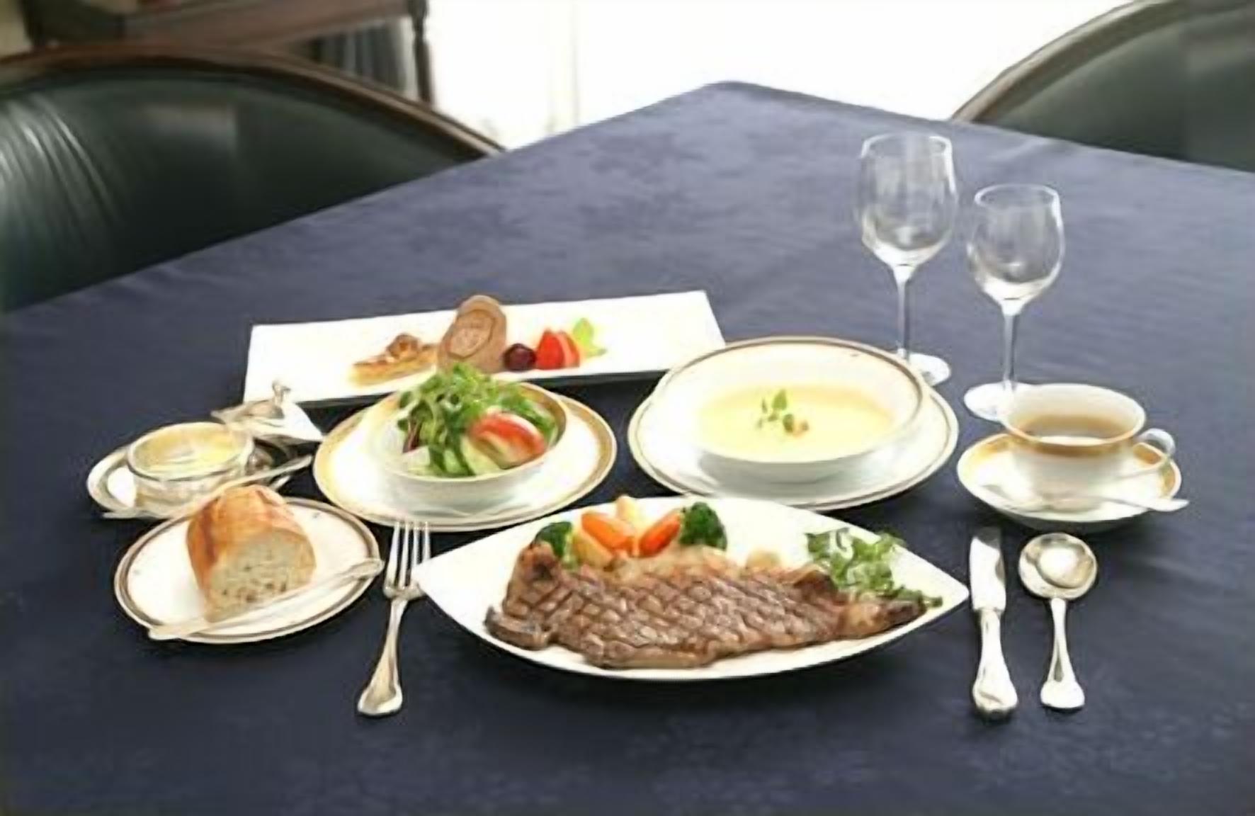 A formal dining table set with various dishes, including fish, salad, soup, and bread, along with wine glasses and cutlery.
