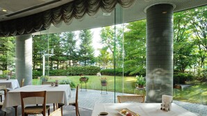 Restaurant amb taules preparades per dinar, una tassa de cafè sobre una taula, i vista a un jardí a través de grans finestres.