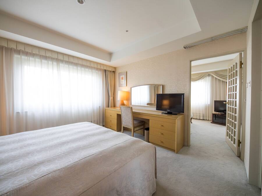 Una habitación de hotel con una cama, un escritorio con computadora, televisor y espejo.