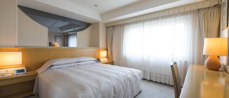 Una habitación de hotel con una cama, lámparas de noche, un escritorio con silla y un ventanal con cortinas.