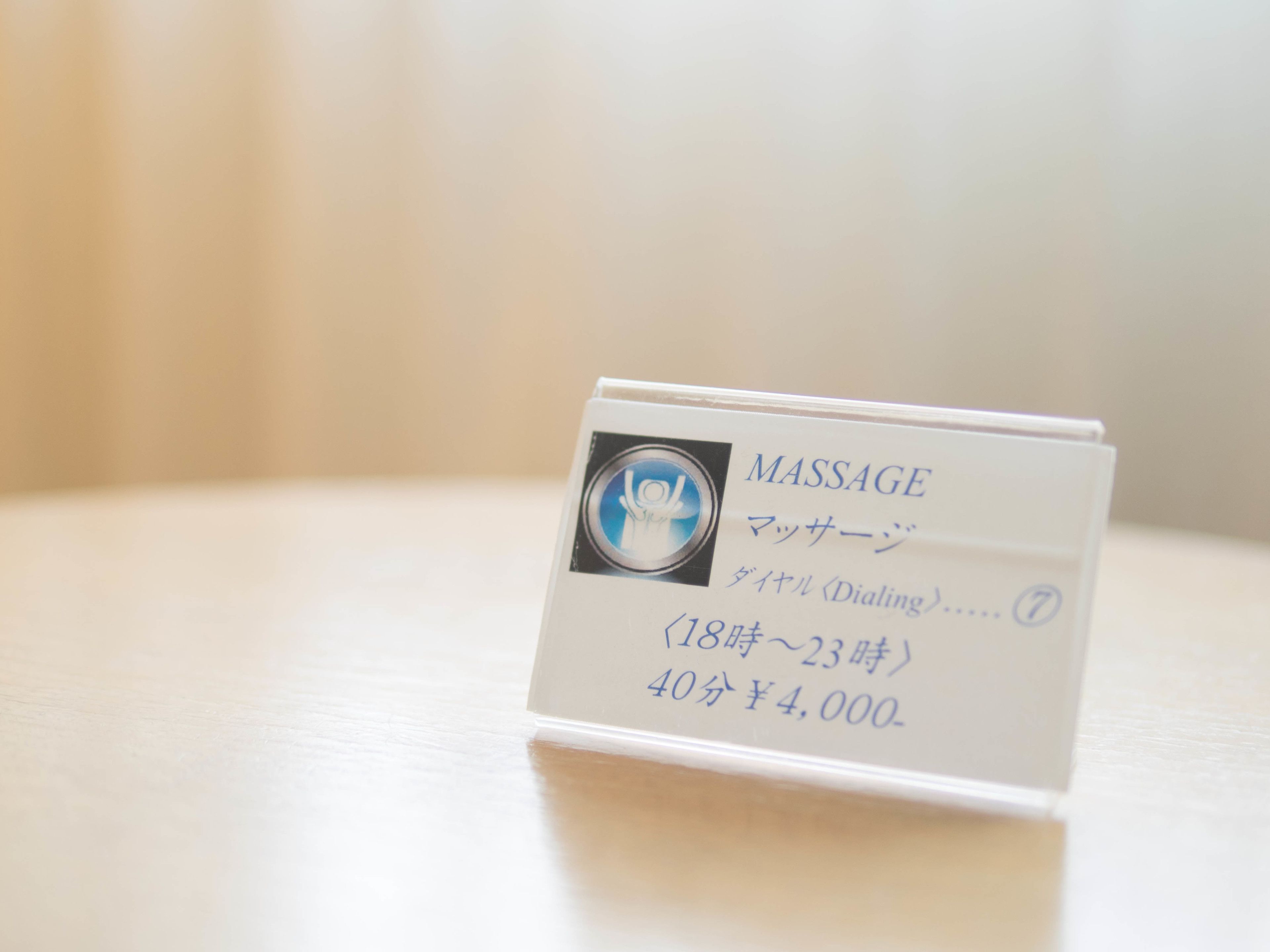 Tarjeta blanca con la palabra "MASSAGE" y caracteres japoneses, que indica un servicio de masaje.