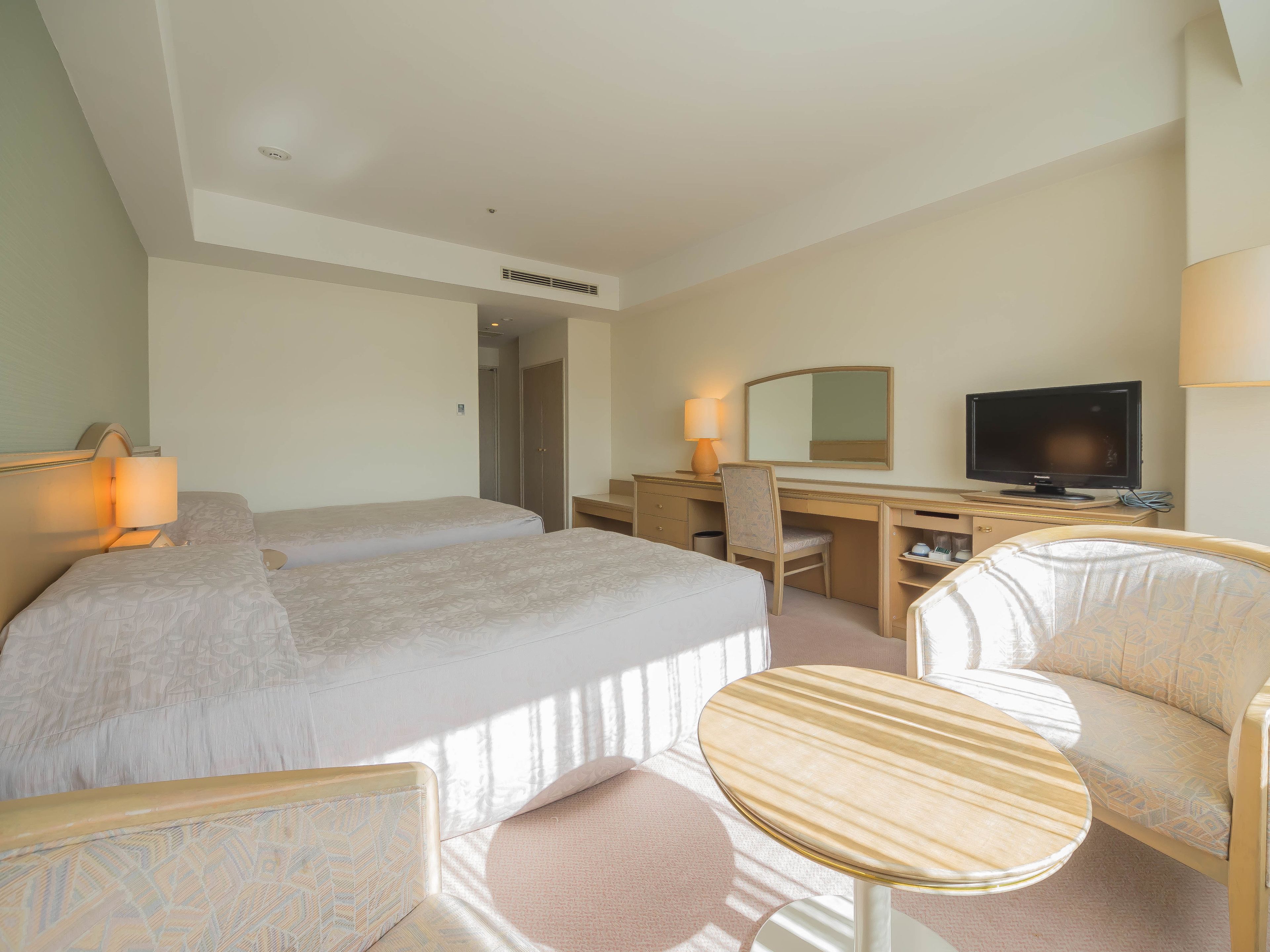 Habitación de hotel con dos camas, un escritorio con computadora, televisor, una silla y una mesita redonda.