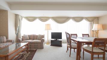 A living room with a sofa, a glass coffee table, a TV, a dining table with chairs, and a carpeted floor.