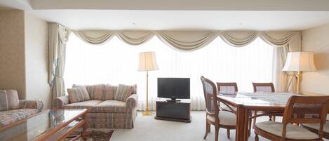 A living room with a sofa, a glass coffee table, a TV, a dining table with chairs, and a carpeted floor.