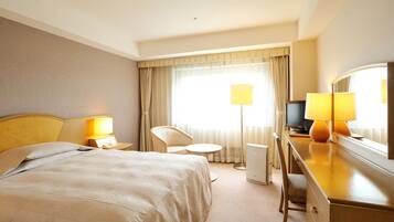 Habitación de hotel con cama, escritorio, silla, televisor y lámpara.