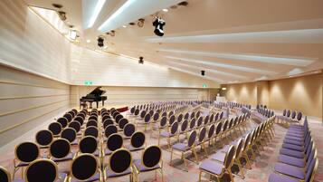A conference room with rows of purple chairs and a grand piano in the background.