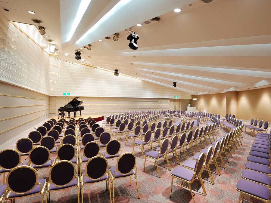 A conference room with rows of purple chairs and a grand piano in the background.