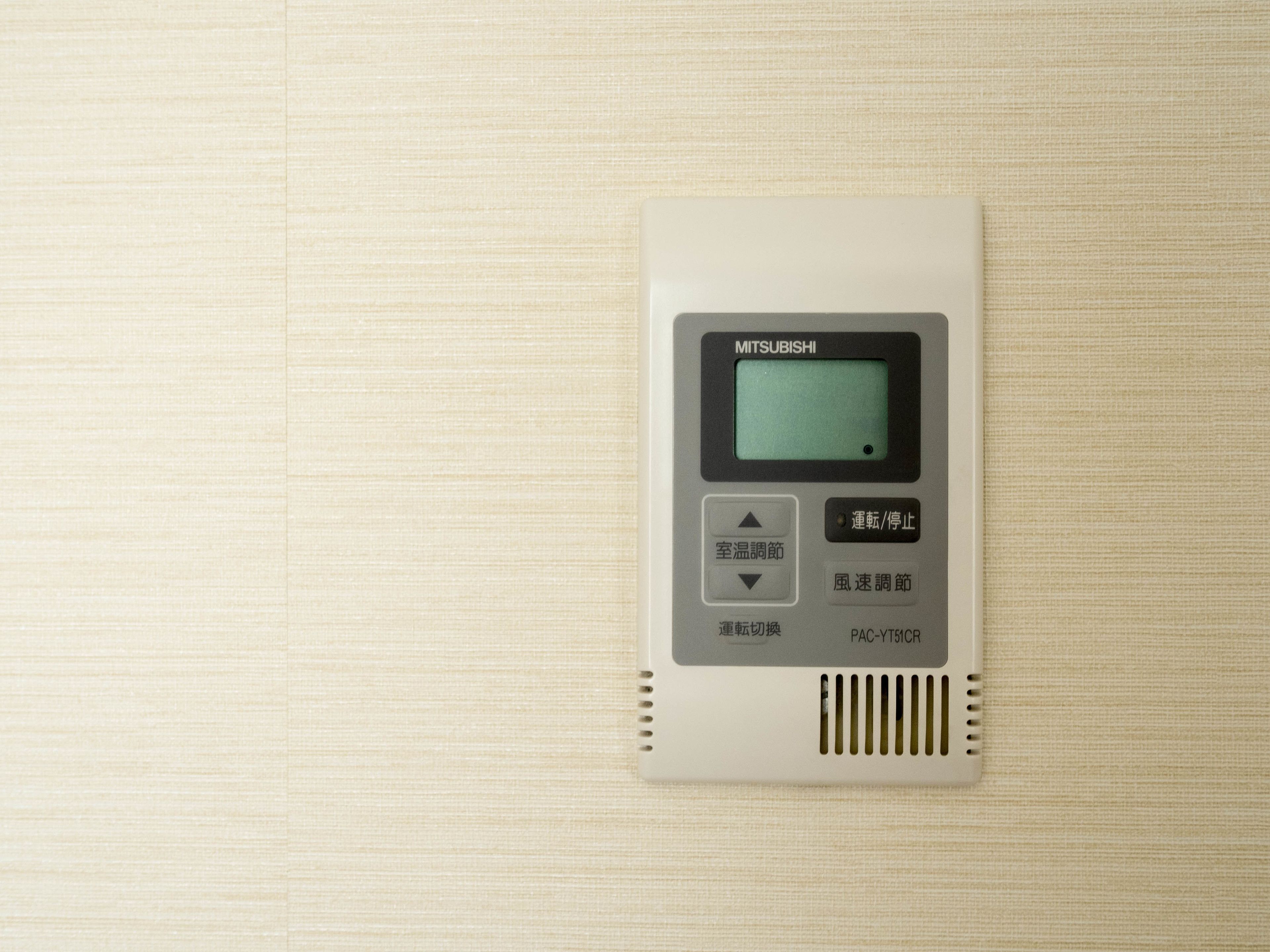 A control panel with Mitsubishi branding, featuring buttons for room temperature and fan speed adjustments.
