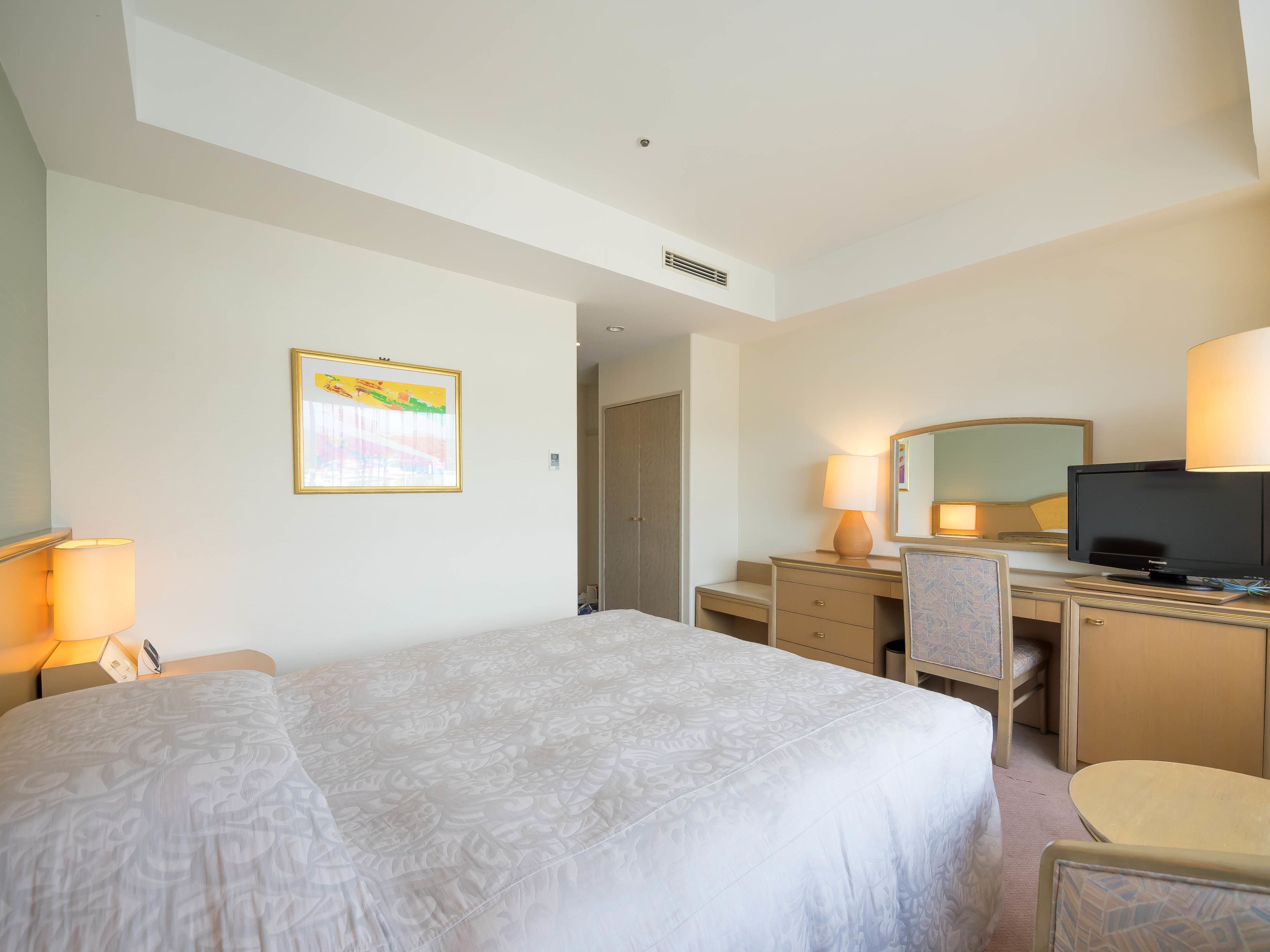Una habitación de hotel con una cama grande, un escritorio con computadora, una silla, televisor y lámpara.
