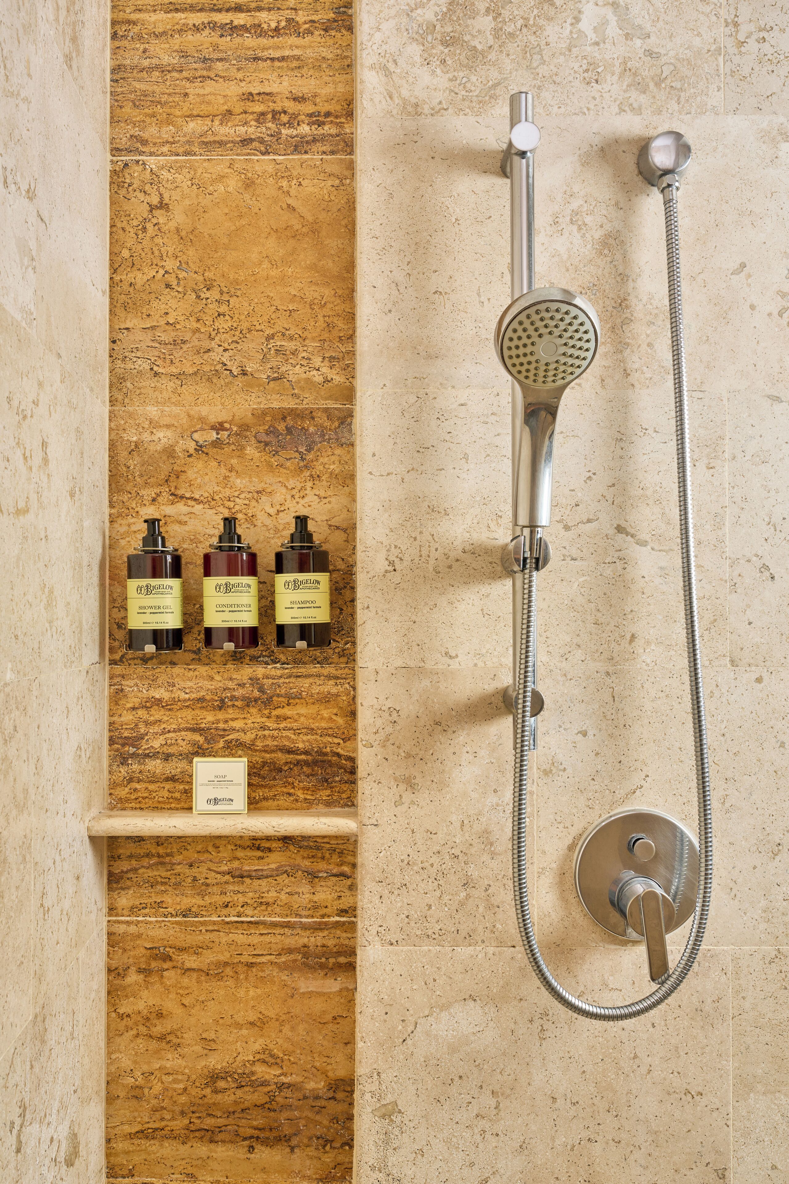 A bathroom with a shower, a shelf with three bottles of toiletries, and a control panel.