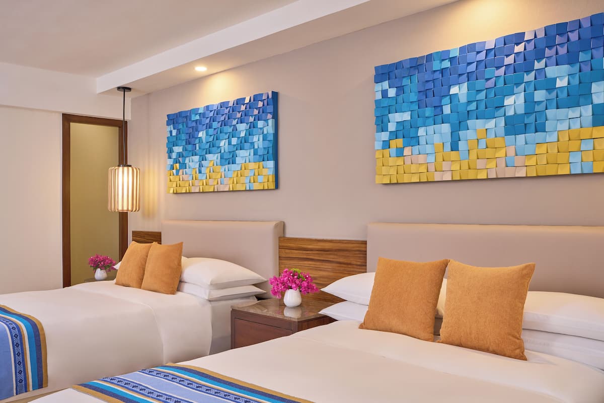 Habitación de hotel con dos camas, cabecera de madera, mesita de noche con un florero y una obra de arte en la pared.