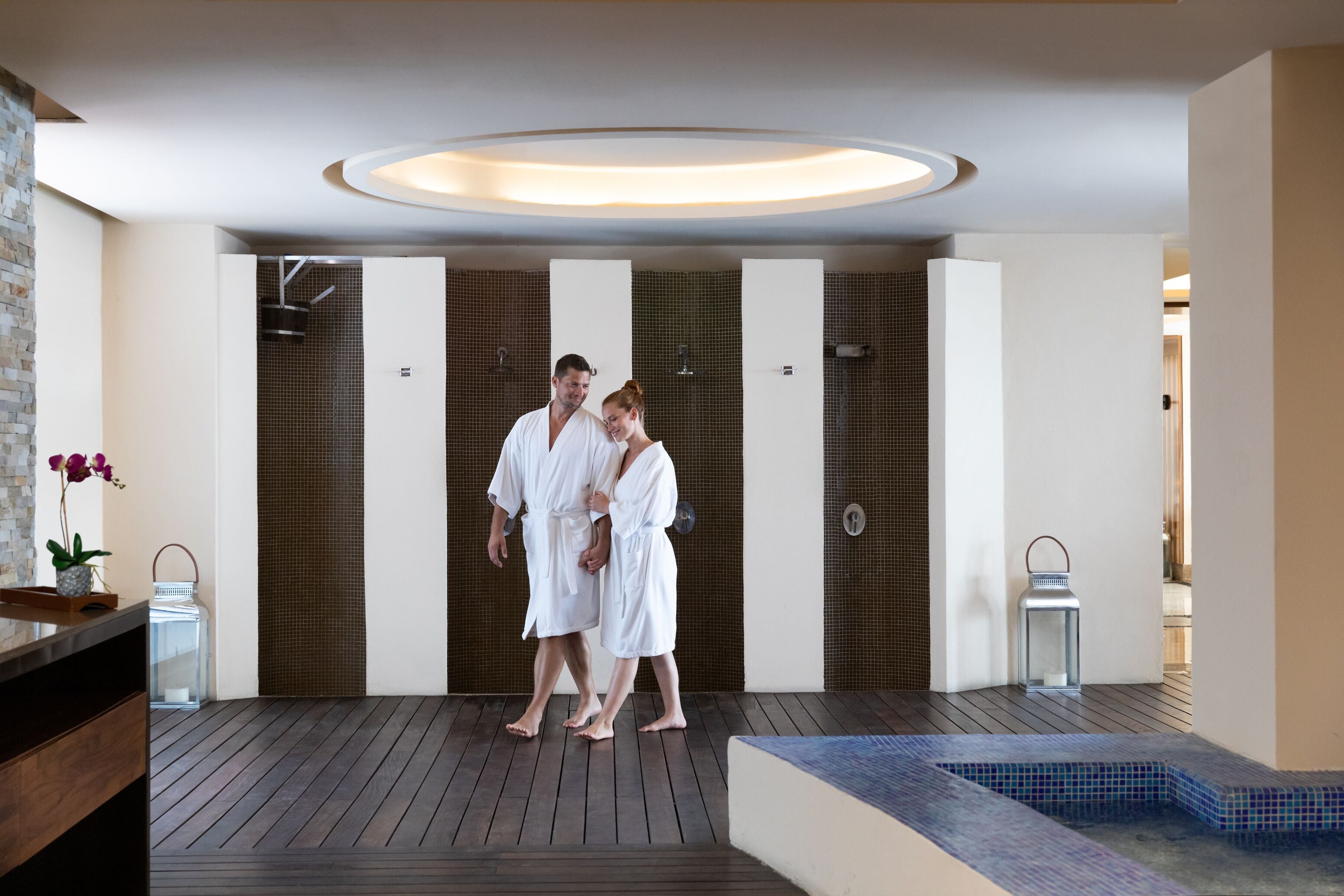A modern spa area with a wooden floor, a small pool, and a row of private changing rooms.