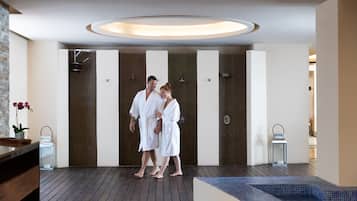 A modern spa area with a wooden floor, a small pool, and a row of private changing rooms.