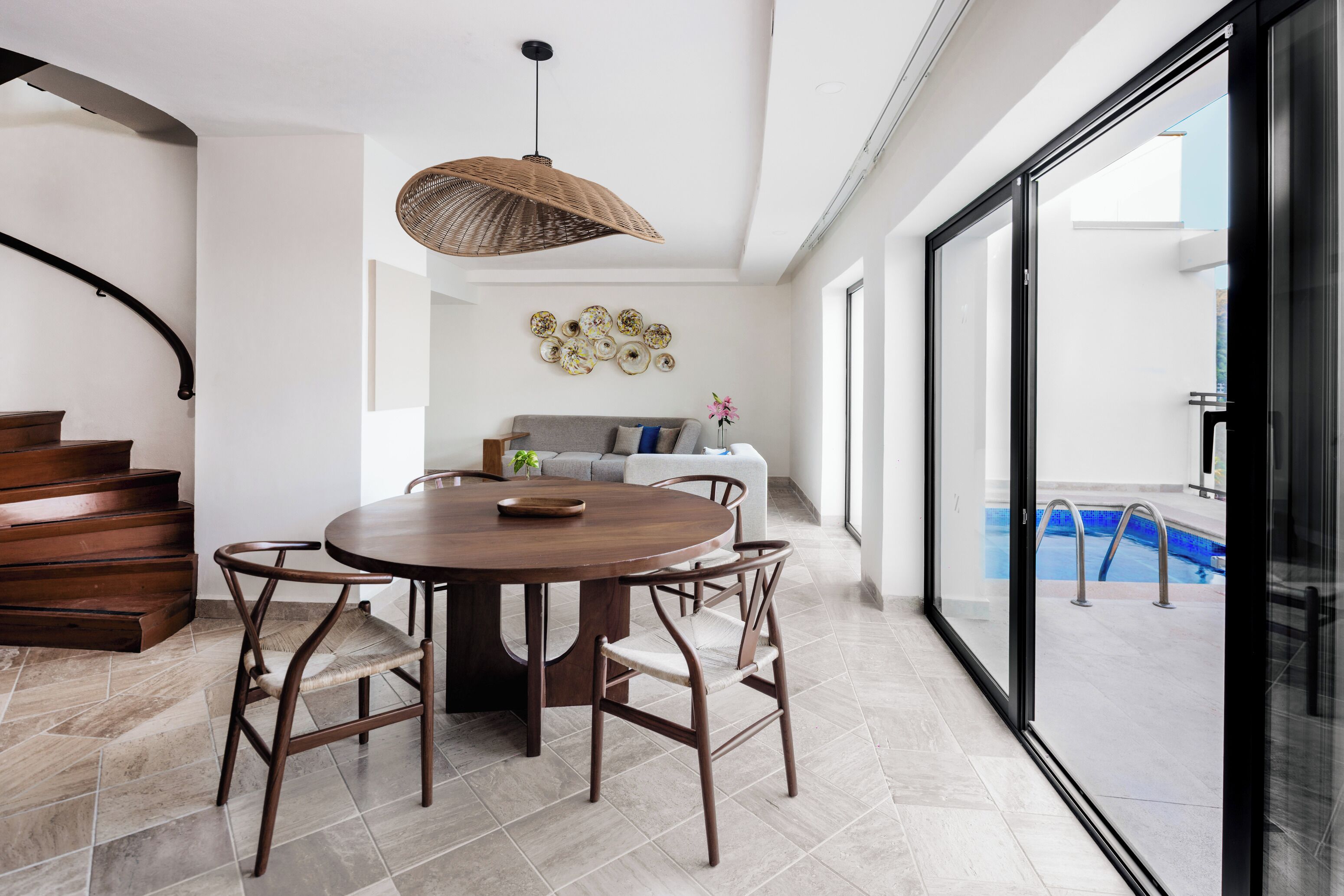 A modern dining area with a round wooden table, four chairs, and a woven ceiling light.