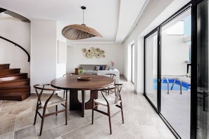 A modern dining area with a round wooden table, four chairs, and a woven ceiling light.