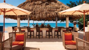 Un bar junto a la playa con sillas de mimbre y sombrillas de paja, con vista al océano.