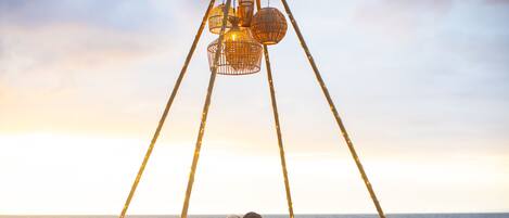 A beach setting with a canopy, wicker furniture, and a table with drinks.