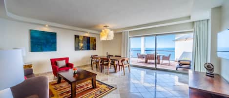 A spacious living area with a dining set, a red armchair, and a large window offering a view of the sea.