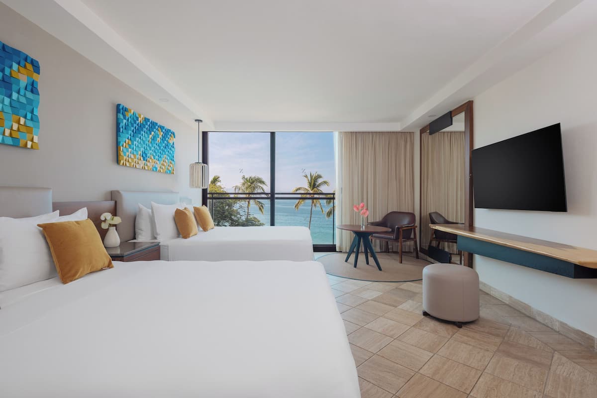 Habitación de hotel con dos camas, un escritorio, un televisor y vista al océano.